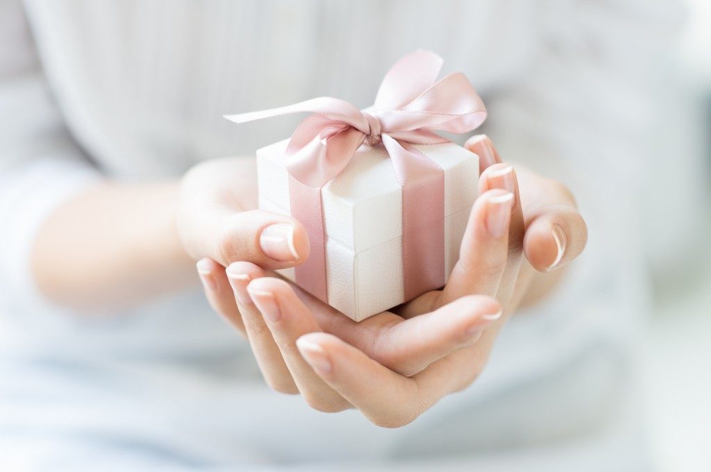 Close up shot of female hands holding a small gift wrapped with pink ribbon.